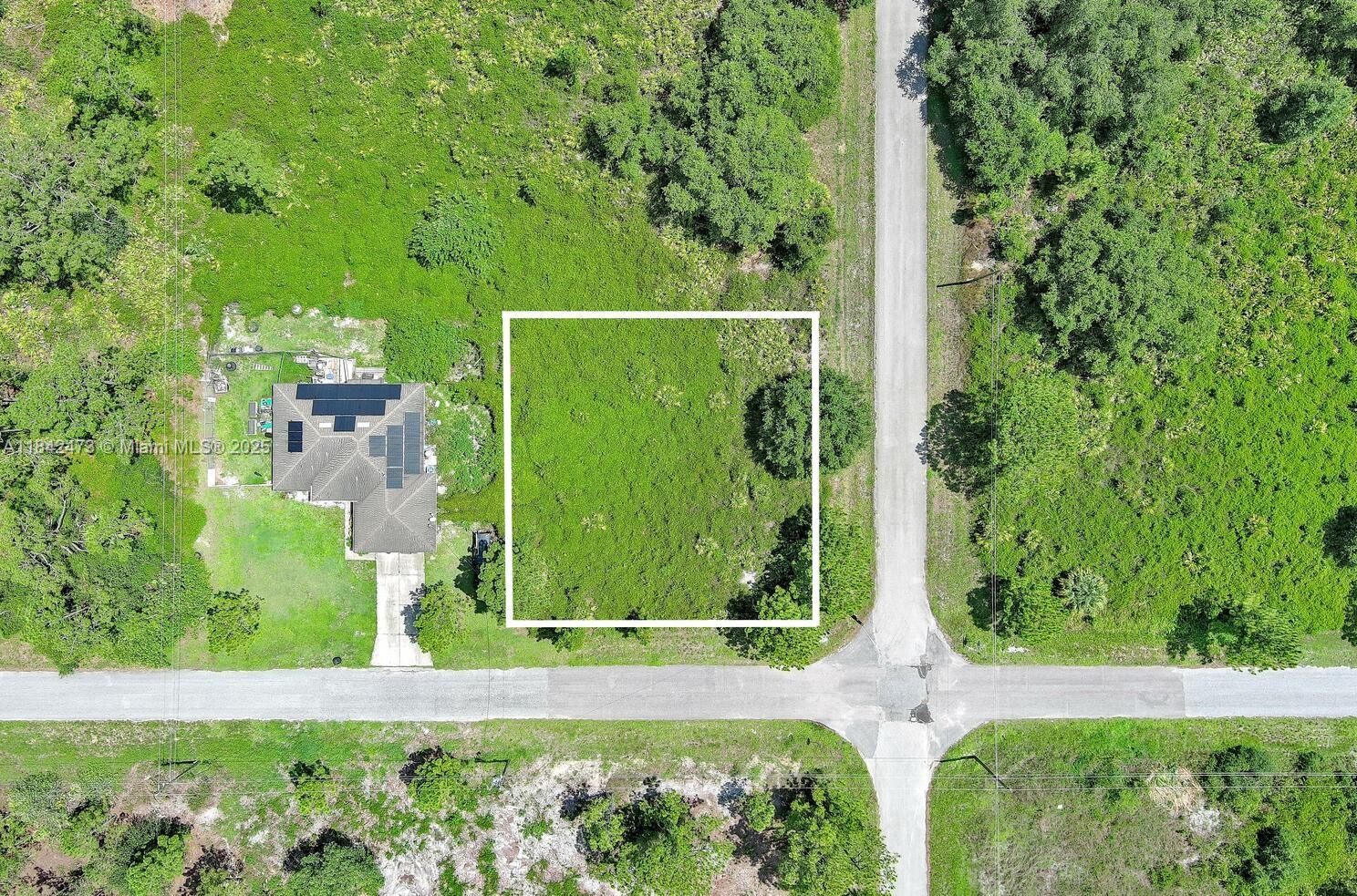 An aerial view shows a vacant, square-outlined lot adjacent to a house with solar panels — 3100 E 13th St, Lehigh Acres FL 33972, LEHIGH ACRES, FL