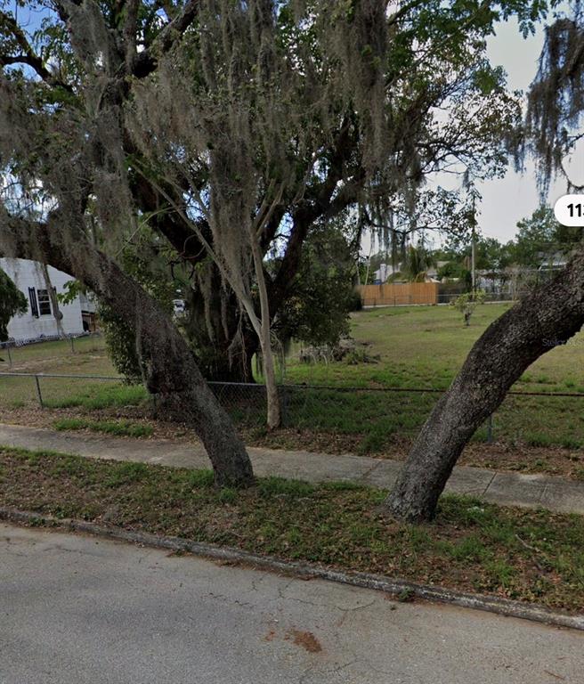 A grassy vacant lot features two large trees in the foreground and a chain-link fence — 1131 EDGEMOOR AVENUE, SEBRING, FL
