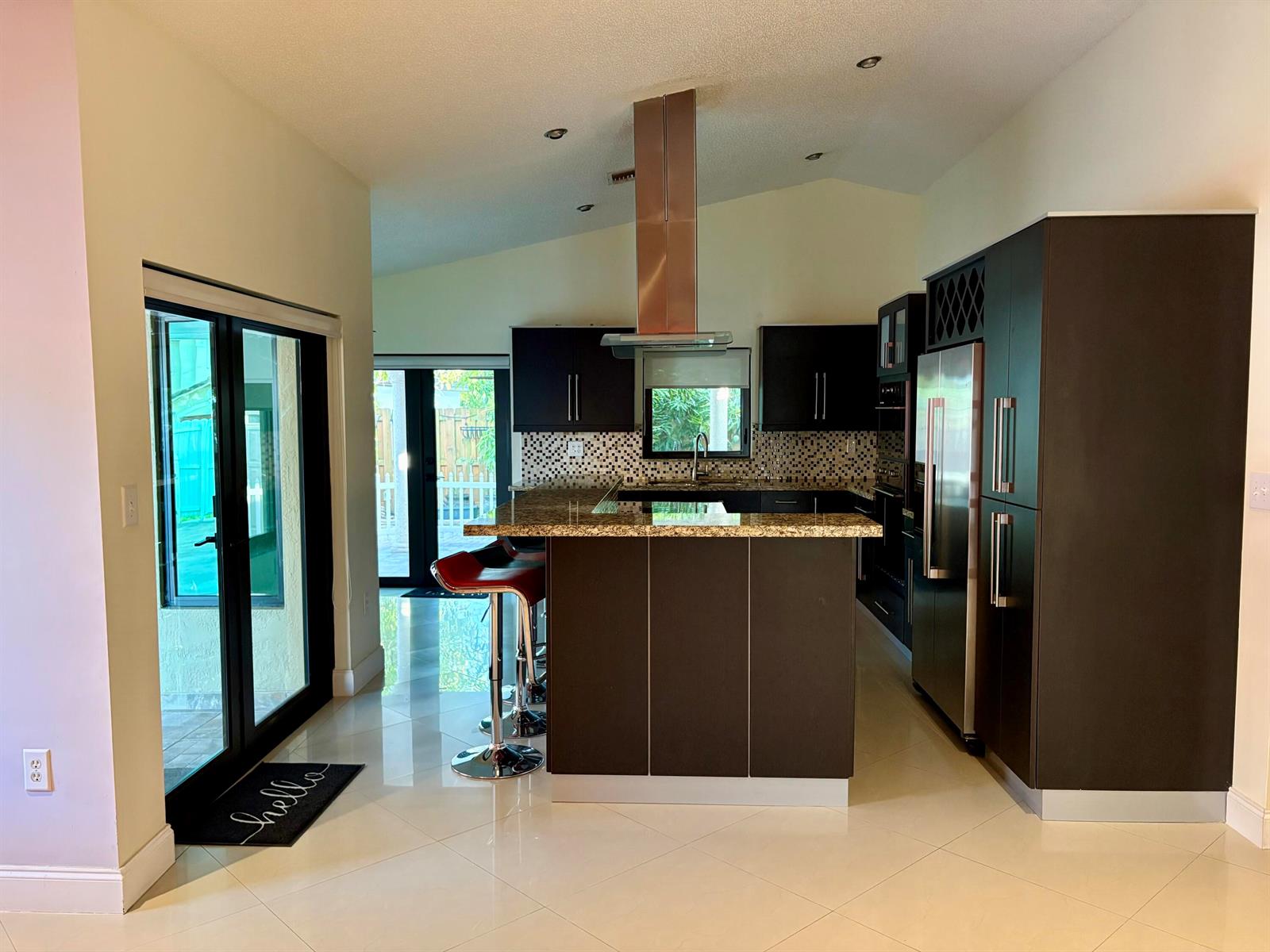 A modern kitchen features dark cabinetry, a granite-topped island with bar stools, and glass doors — 14776 SW 138th Terrace, Miami FL 33196, MIAMI, FL