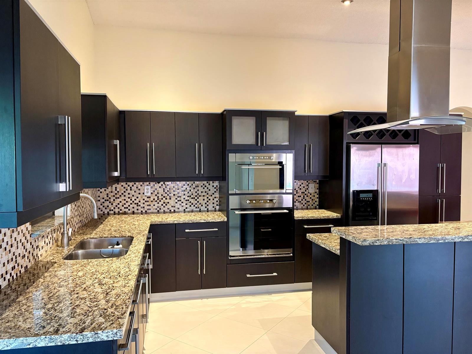 A modern kitchen features dark cabinetry, granite countertops, stainless steel appliances, and a mosaic backsplash — 14776 SW 138th Terrace, Miami FL 33196, MIAMI, FL
