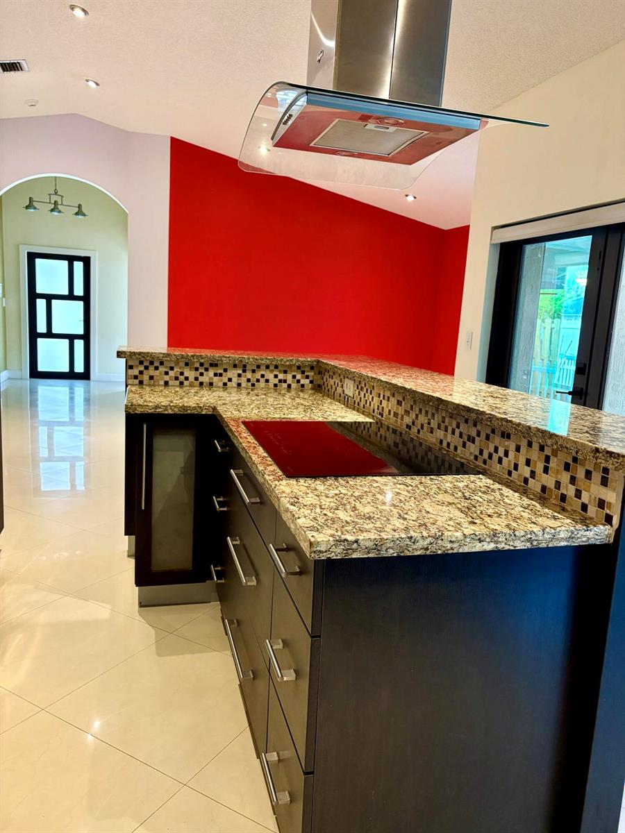 A kitchen island with granite countertops and dark cabinets sits beneath a stainless steel hood — 14776 SW 138th Terrace, Miami FL 33196, MIAMI, FL