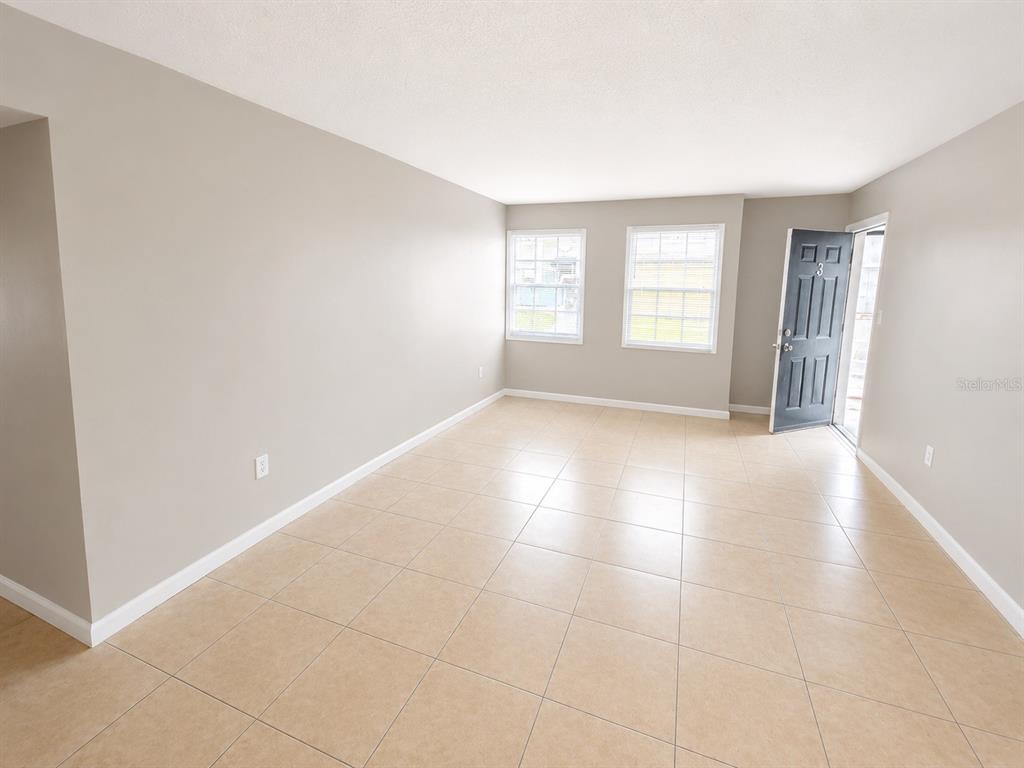 An empty room features light-colored tile flooring, beige walls, two windows, and an open door — 2779 L B MCLEOD ROAD UNIT B, ORLANDO, FL