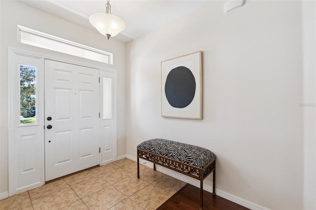 A bright entryway features a white front door, tile flooring, and a zebra-print bench — 26645 MANASSAS DRIVE, LEESBURG, FL