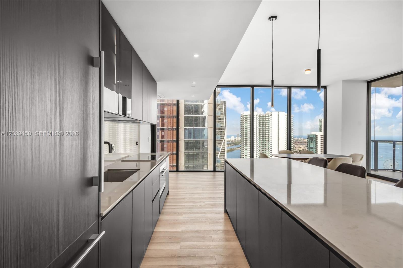 A modern kitchen features dark cabinetry, a large island, and floor-to-ceiling windows with city views — 20 NE 11th St # 5102, Miami FL 33132, MIAMI, FL