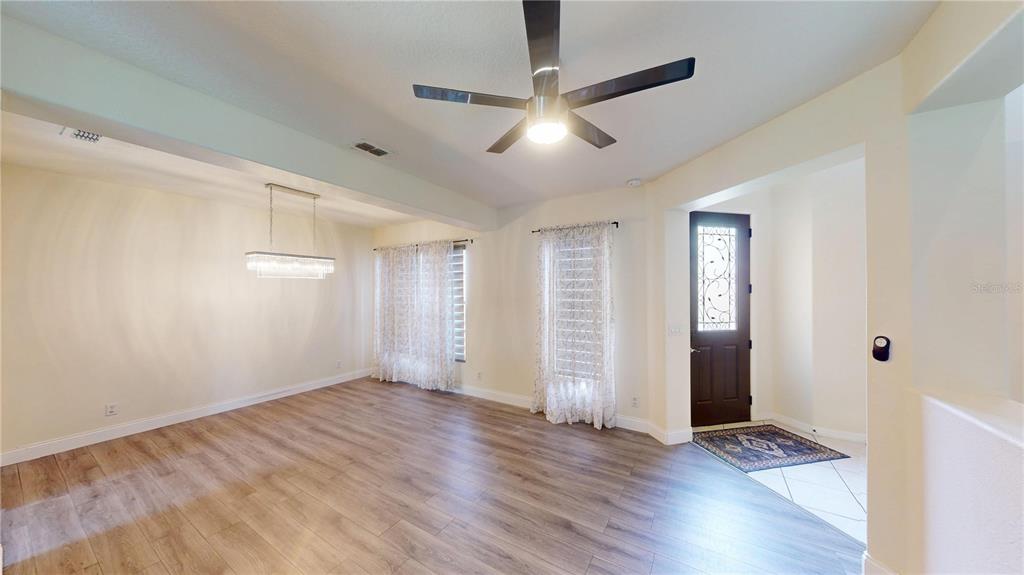 A dining area with wood-look flooring, a modern chandelier, and a ceiling fan near an entryway — 3044 CAMINO REAL DRIVE S, KISSIMMEE, FL