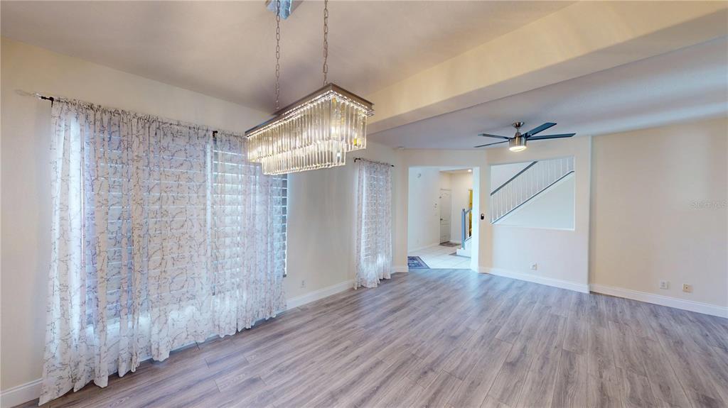 A dining room with light wood-look flooring, a crystal chandelier, and sheer curtains over windows — 3044 CAMINO REAL DRIVE S, KISSIMMEE, FL