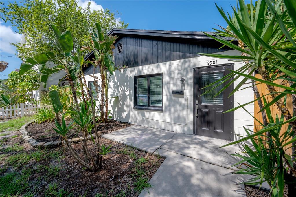 A white concrete block building features a dark door, black trim, and tropical landscaping — 6901 S FITZGERALD STREET, TAMPA, FL