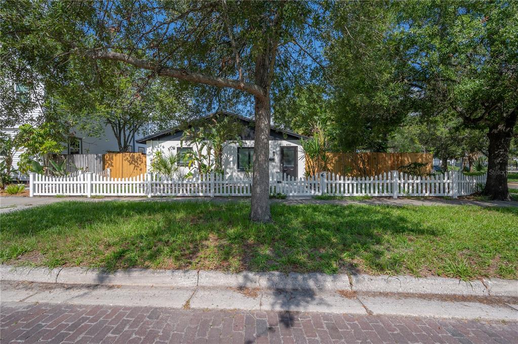 A white house with a dark roof sits behind a white picket fence and trees — 6901 S FITZGERALD STREET, TAMPA, FL