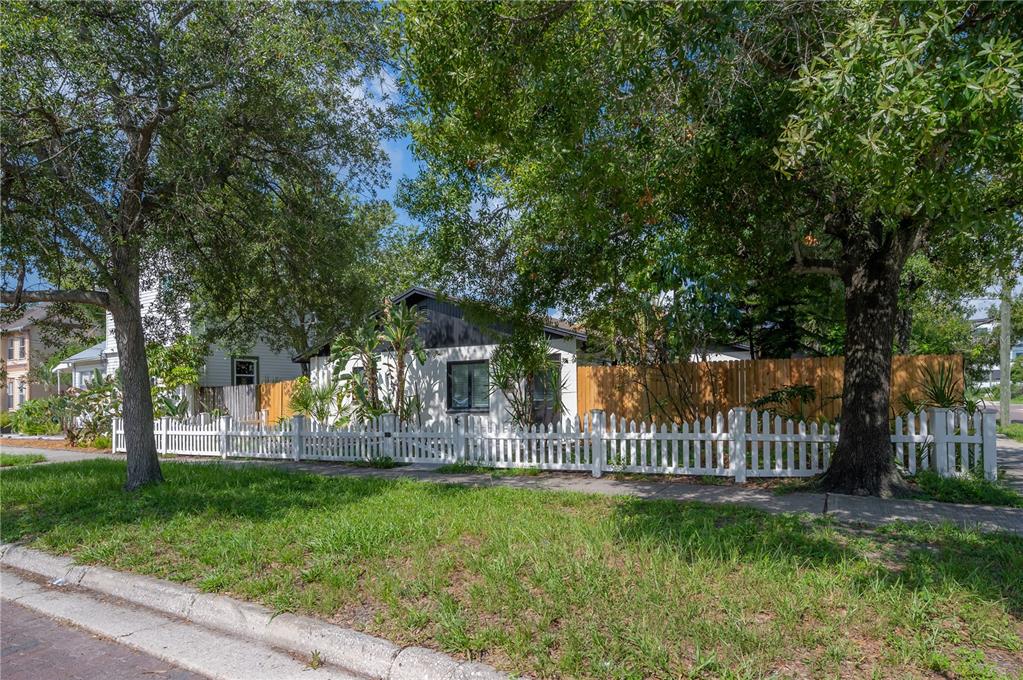 A white house with a picket fence is partially obscured by large trees — 6901 S FITZGERALD STREET, TAMPA, FL