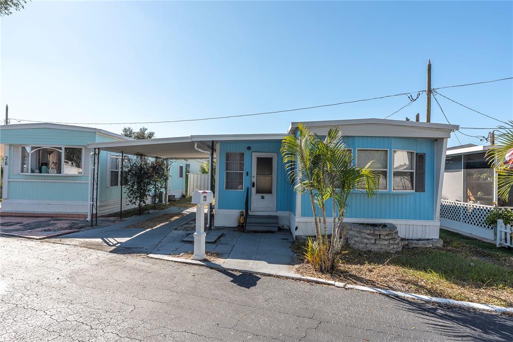 A light blue mobile home features a carport, a front door, and a small palm tree — 7801 34TH AVENUE N UNIT 27, ST PETERSBURG, FL