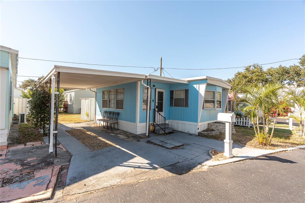 A light blue mobile home features a carport, a front entrance, and a paved driveway — 7801 34TH AVENUE N UNIT 27, ST PETERSBURG, FL
