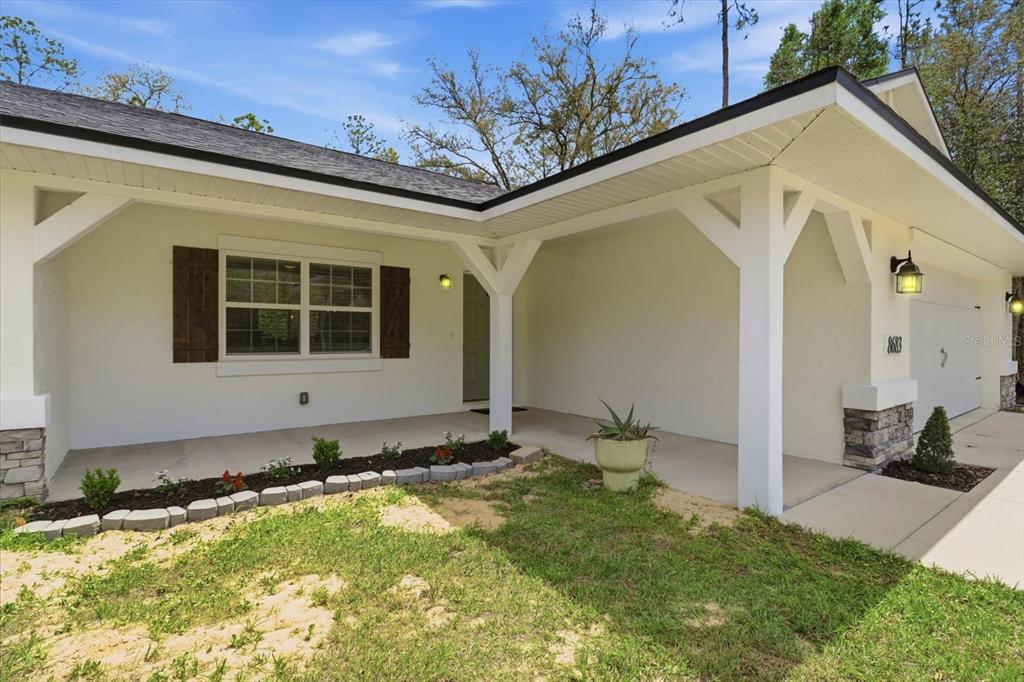A white house exterior features a covered front porch, stone accents, and dark wood shutters — 8683 N TEATHER TERRACE, DUNNELLON, FL