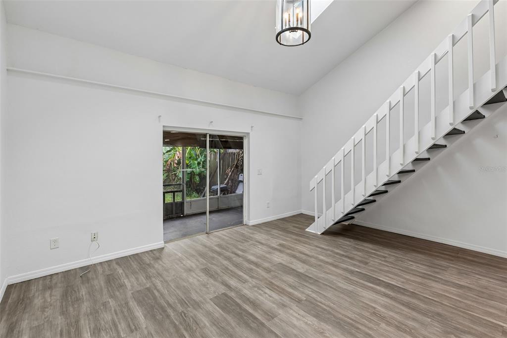 A living room features wood-look flooring, a white staircase, and a sliding glass door — 2835 HUNT CLUB LANE, ORLANDO, FL