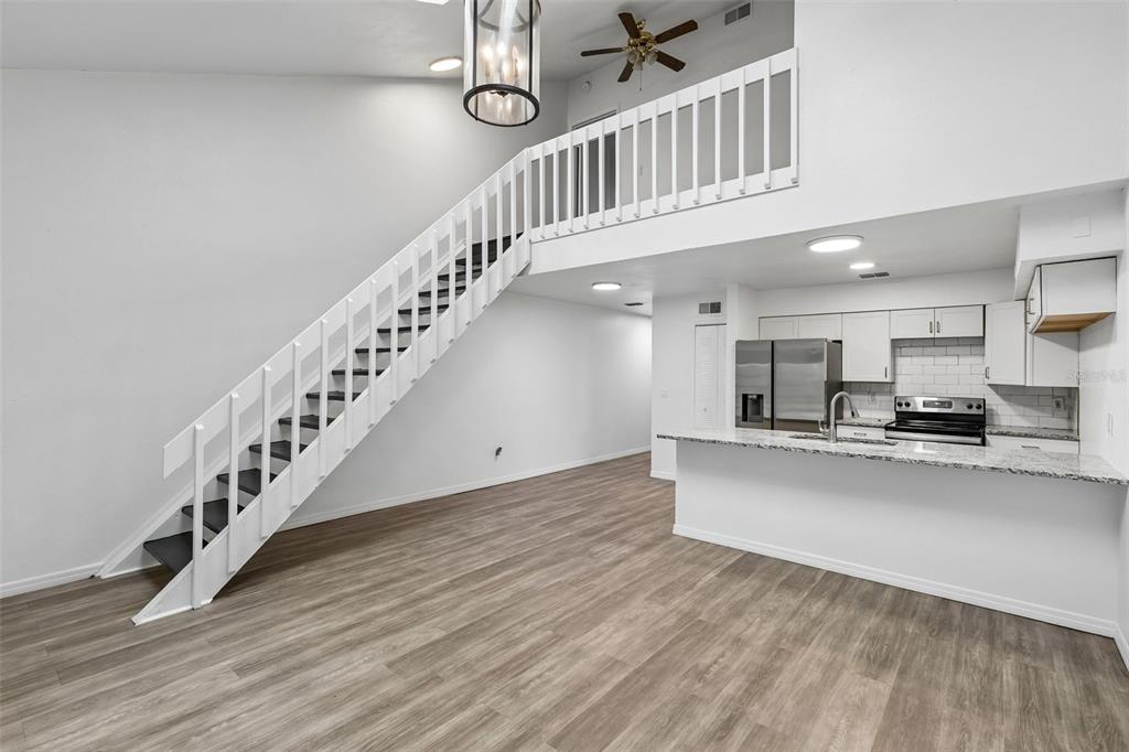 A living area with wood-look flooring, a white staircase, and an open kitchen with granite countertops — 2835 HUNT CLUB LANE, ORLANDO, FL