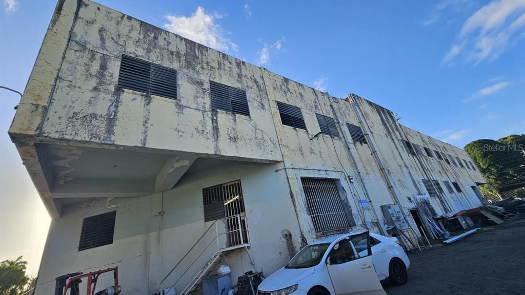 A low-angle exterior view of a weathered, multi-story industrial building with a white car parked — Ramon B. Lopez GAZTAMBIDE ST., SAN JUAN, PR