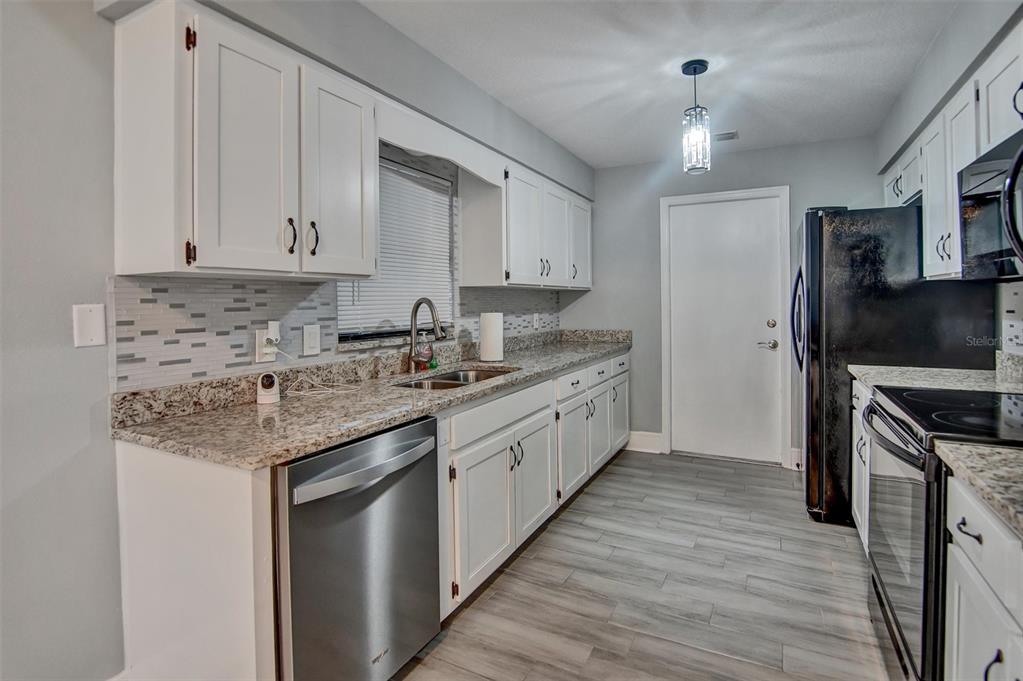 A kitchen features white cabinets, granite countertops, stainless steel appliances, and light wood-look flooring — 2728 COURTLAND BOULEVARD, DELTONA, FL