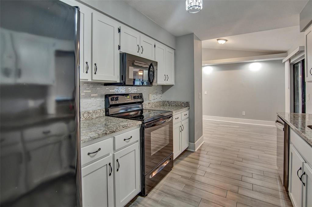 A kitchen features white cabinets, granite countertops, stainless steel appliances, and light wood-look flooring — 2728 COURTLAND BOULEVARD, DELTONA, FL