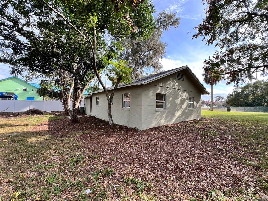 A beige, single-story concrete block house sits on a grassy lot with mature trees — 107 OAKLAND DRIVE, DELAND, FL