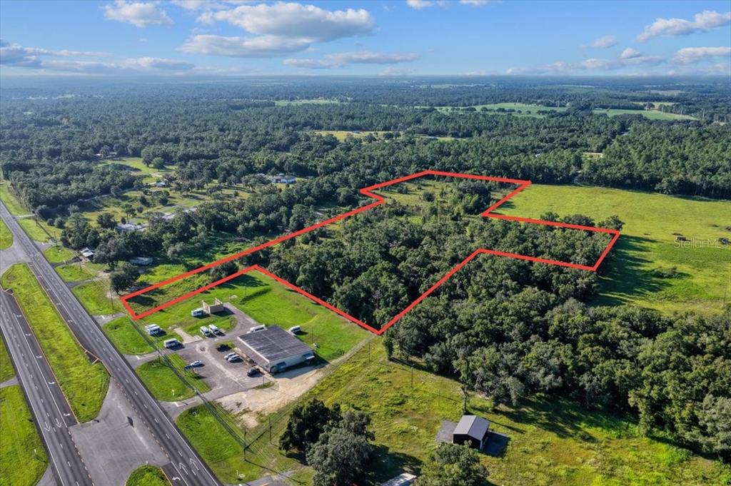 An aerial view shows a rectangular commercial building next to a large, wooded, undeveloped lot — NE HWY 27TH, BRONSON, FL