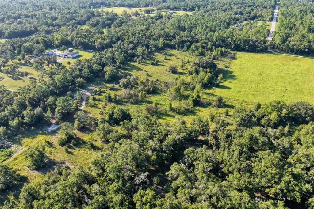 An aerial view shows a large, wooded plot of land with a grassy field and buildings — NE HWY 27TH, BRONSON, FL