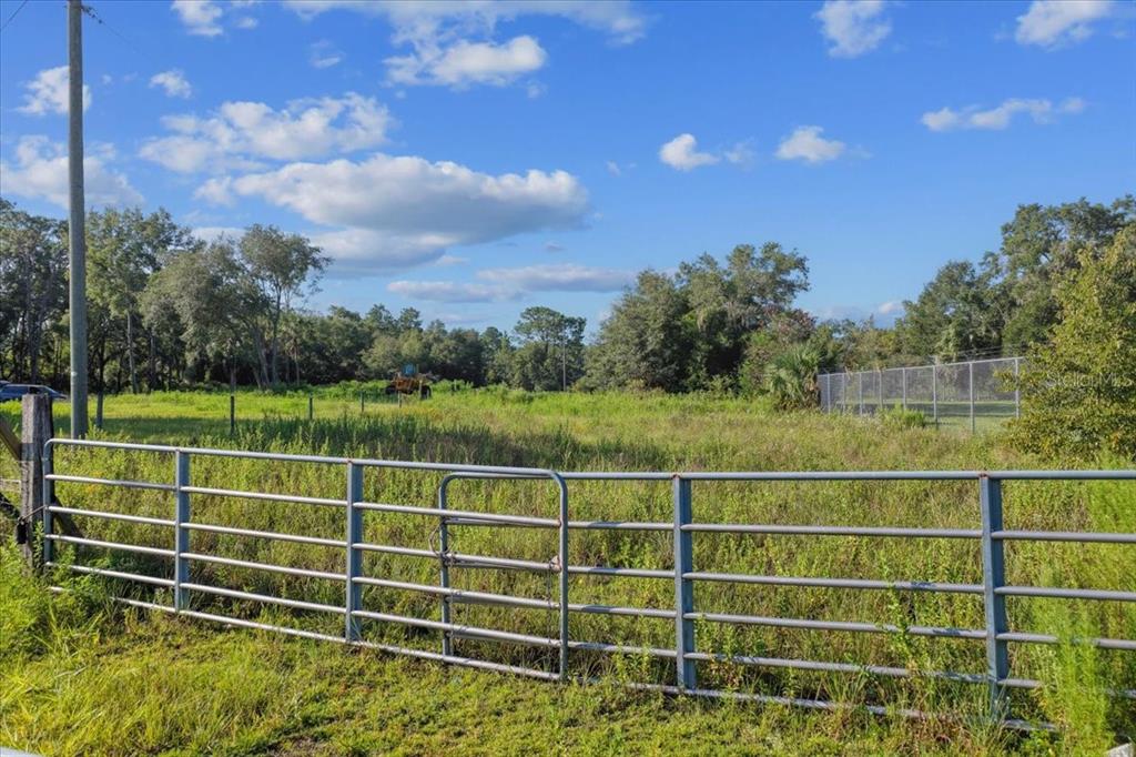 A metal gate opens to a grassy, fenced-in lot with trees under a blue sky — NE HWY 27TH, BRONSON, FL