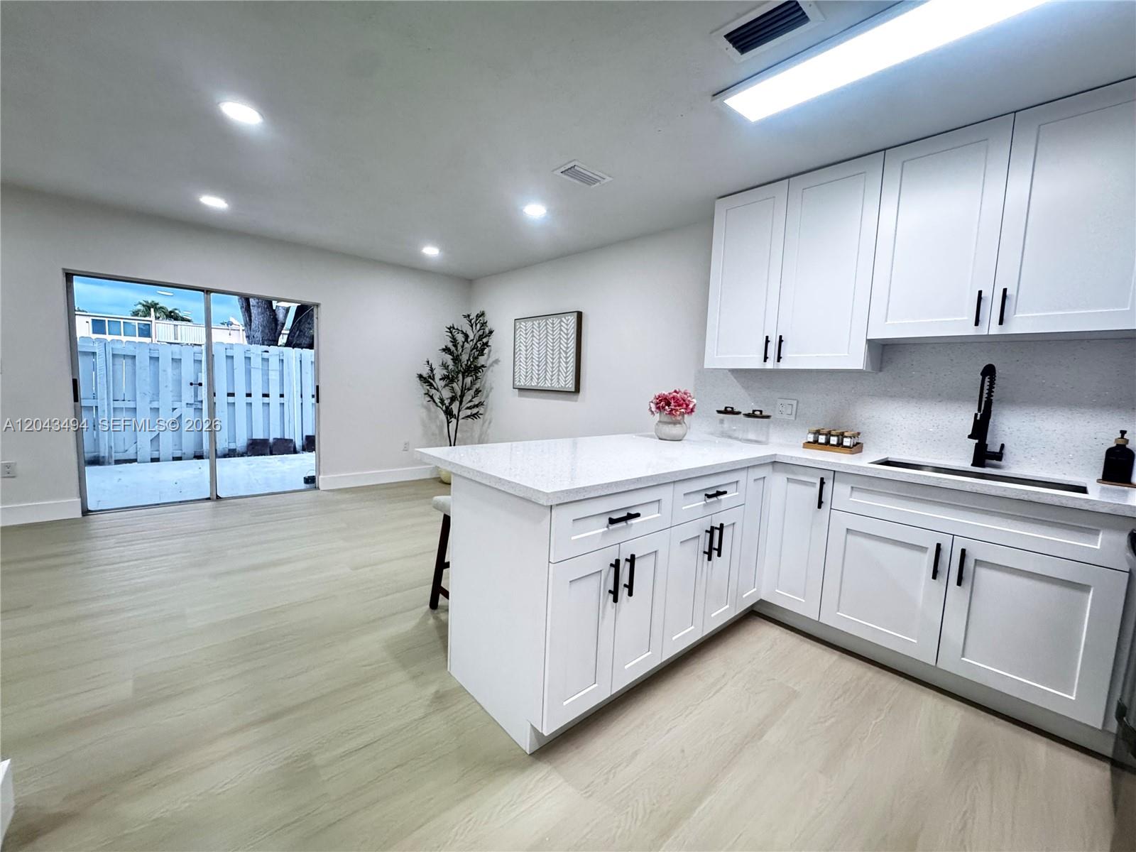 A kitchen features white cabinetry, quartz countertops, and a sliding glass door leading outside — 6350 SW 139th Ave, Miami FL 33183, MIAMI, FL