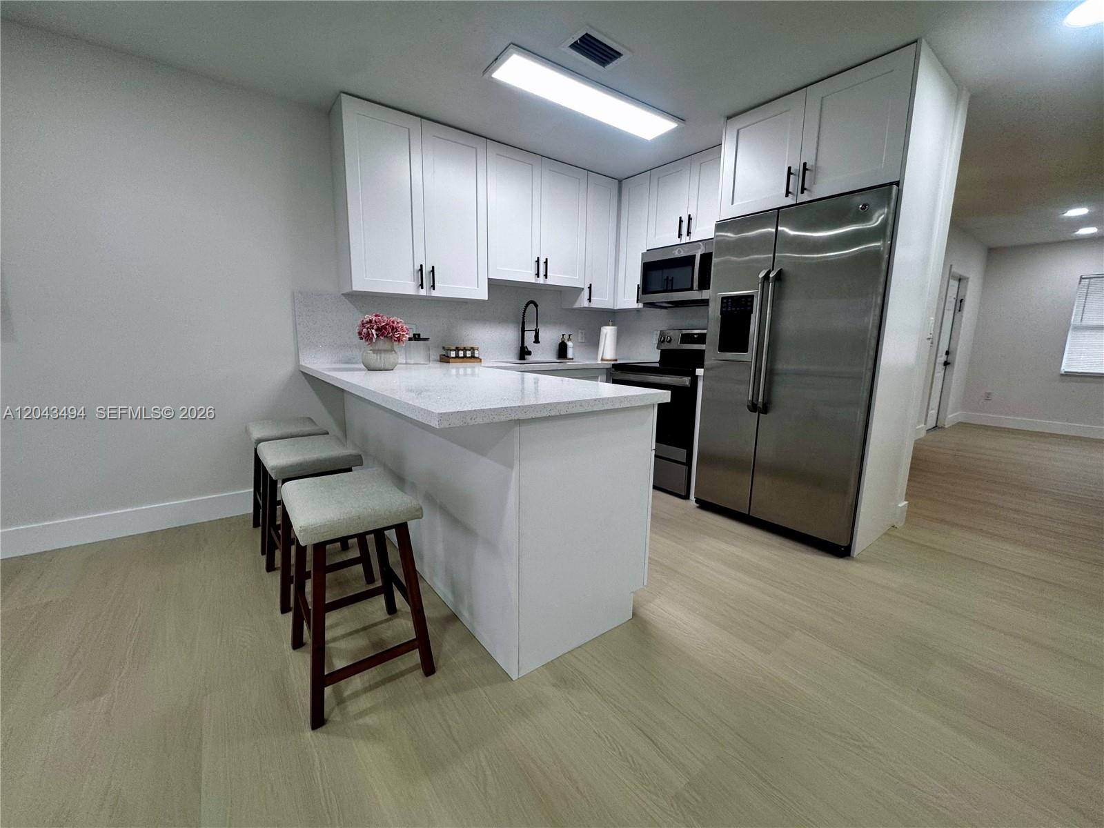 A modern kitchen features white cabinetry, stainless steel appliances, and a breakfast bar with stools — 6350 SW 139th Ave, Miami FL 33183, MIAMI, FL