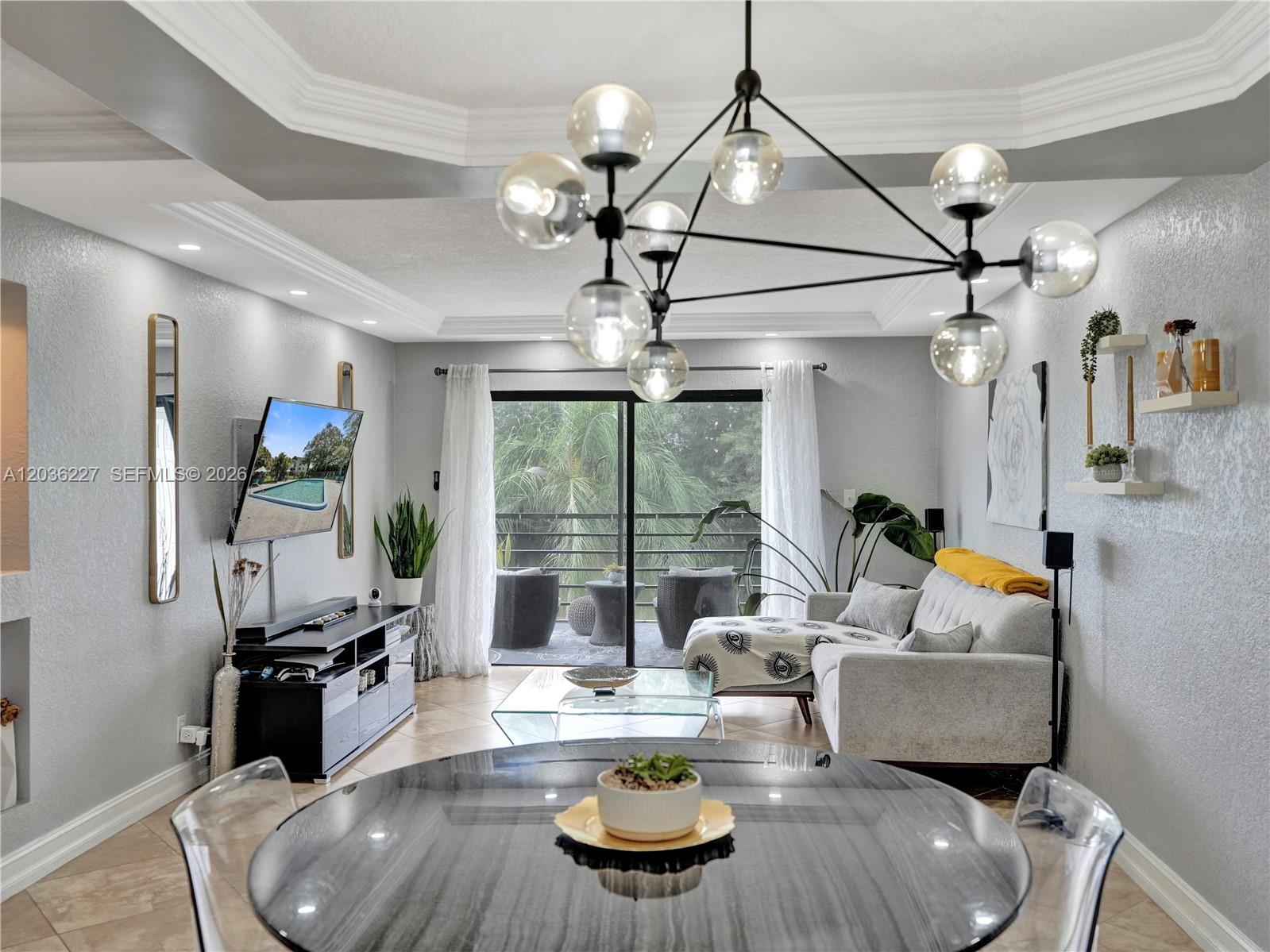 A living room and dining area feature a modern chandelier, gray walls, and a balcony — 9440 SW 8th St # 309, Boca Raton FL 33428, BOCA RATON, FL