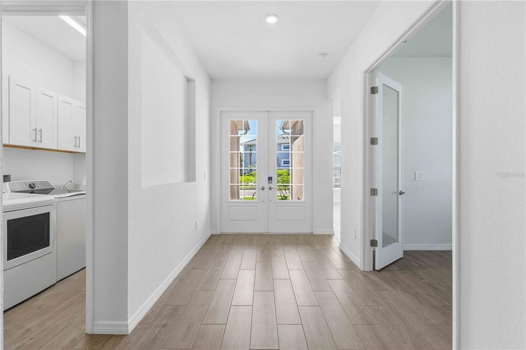 A bright entryway features light wood-look tile flooring, double glass doors, and an adjacent laundry room — 5420 LIGHTNING WHELK LANE, BRADENTON, FL