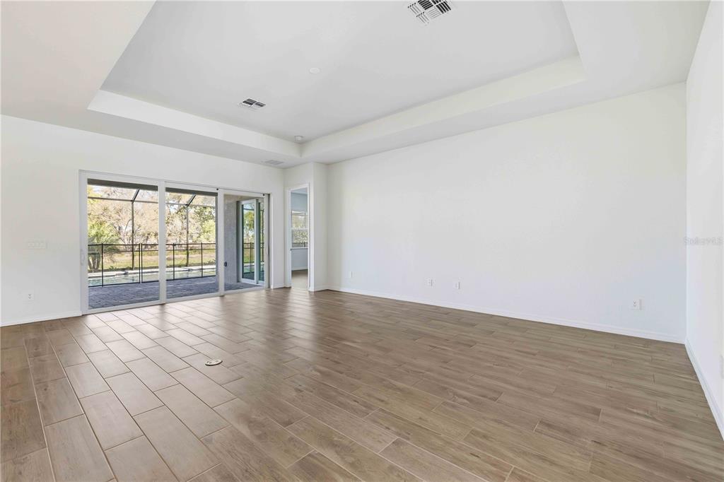 An empty living room features wood-look tile flooring, a tray ceiling, and sliding glass doors — 5420 LIGHTNING WHELK LANE, BRADENTON, FL