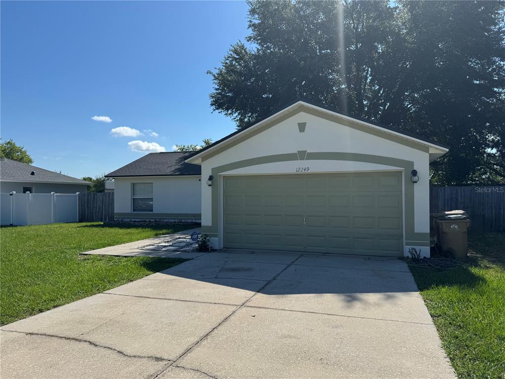 A single-story house features a light-colored exterior, a green garage door, and a concrete driveway — 12249 WOODGLEN CIRCLE, CLERMONT, FL