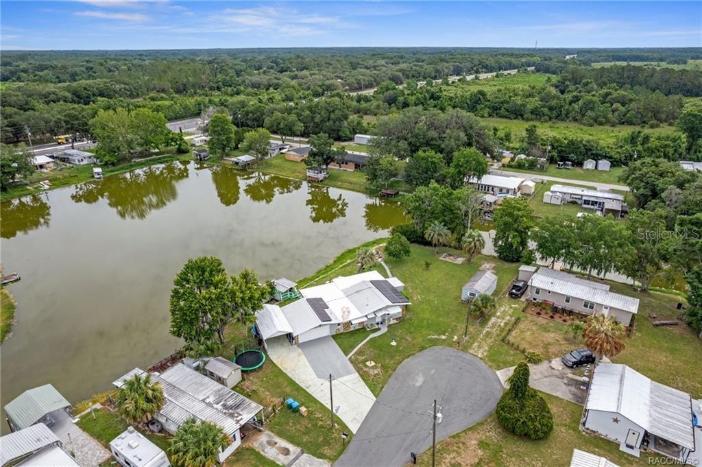 An aerial view shows a house with solar panels, a driveway, and a backyard pond — 10115 E PERCH COURT, INVERNESS, FL