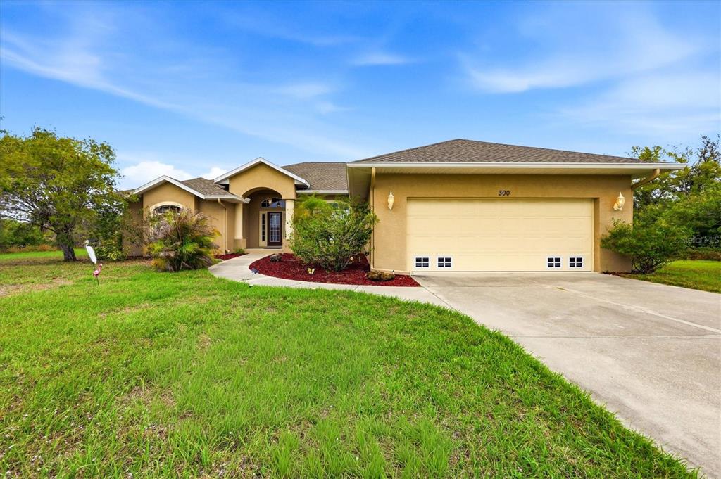 A single-story tan house with a two-car garage and a concrete walkway sits on grass — 300 BAYTREE DRIVE, ROTONDA WEST, FL