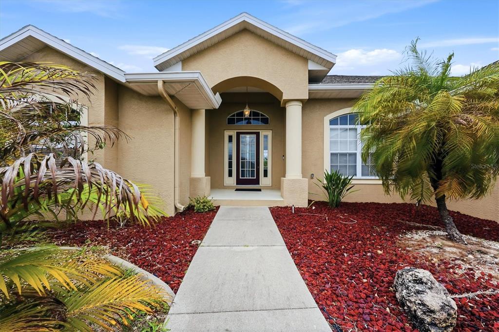 The exterior of a tan house features a covered entryway with columns and red landscaping — 300 BAYTREE DRIVE, ROTONDA WEST, FL