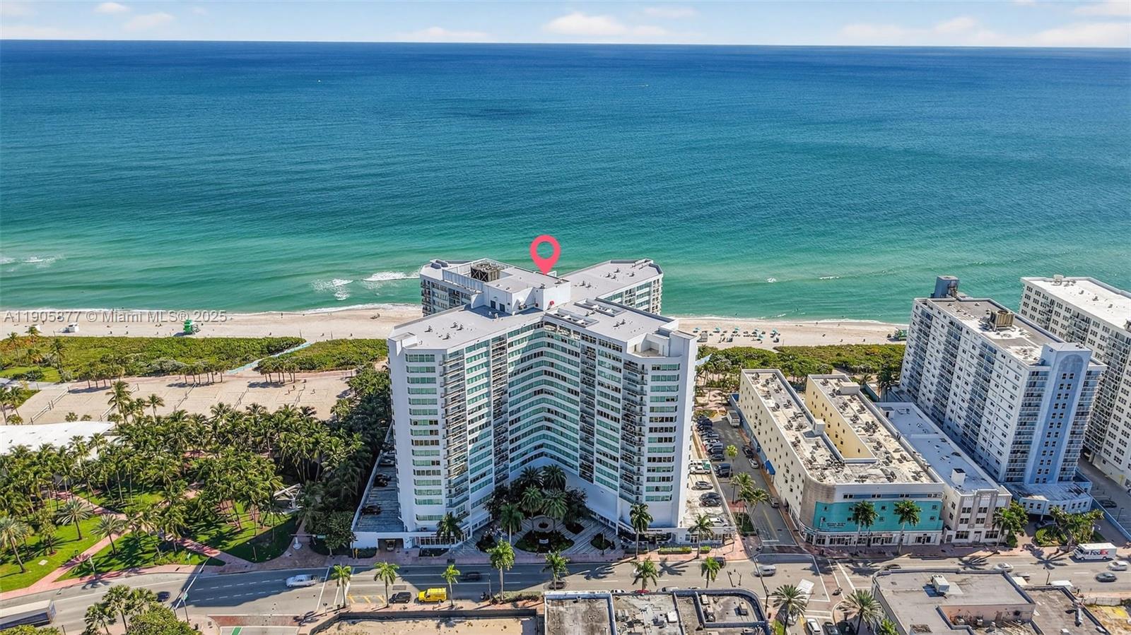 An aerial view shows a large white apartment building situated directly on a sandy beach — 7135 Collins Ave # 705, Miami Beach FL 33141, MIAMI BEACH, FL