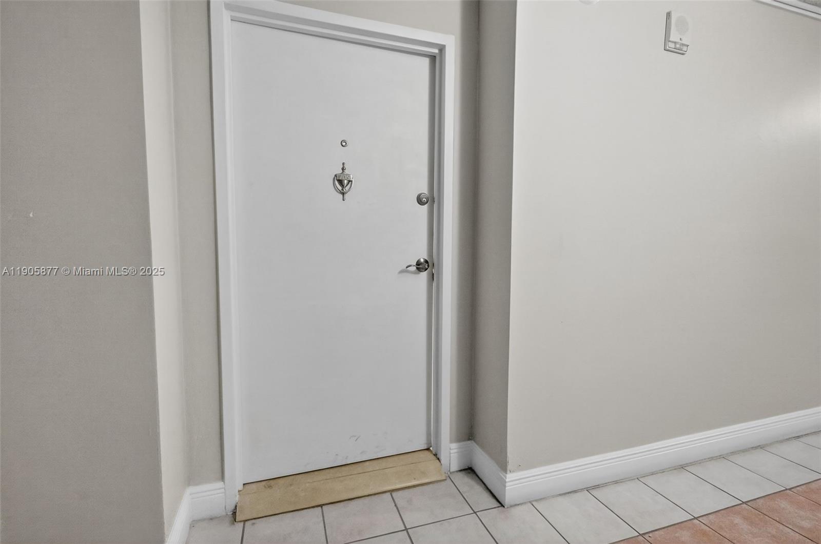A white door with a silver knocker and handle is set in a neutral-walled hallway — 7135 Collins Ave # 705, Miami Beach FL 33141, MIAMI BEACH, FL