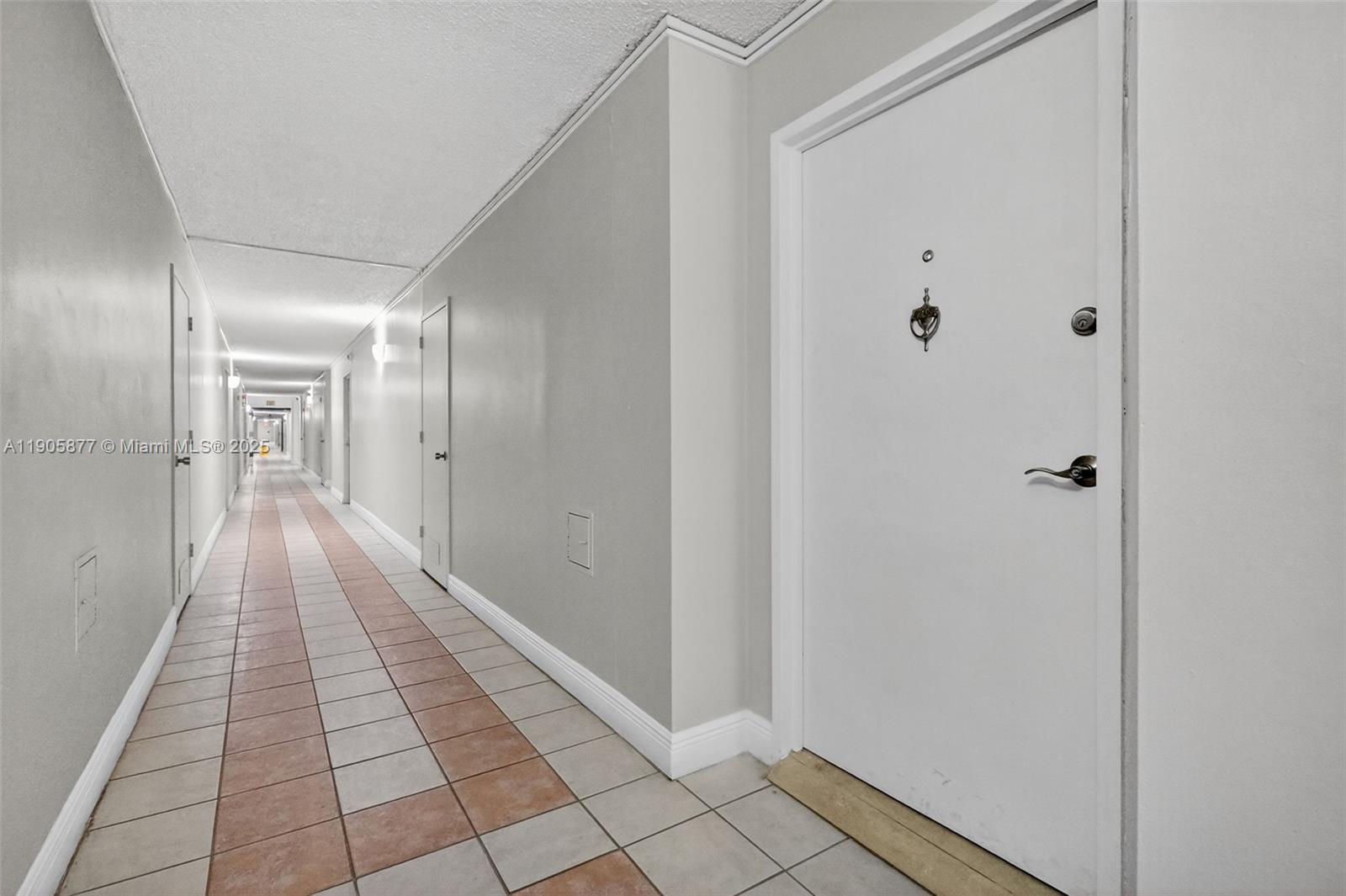 A long, narrow apartment hallway features white doors, light gray walls, and tiled flooring — 7135 Collins Ave # 705, Miami Beach FL 33141, MIAMI BEACH, FL