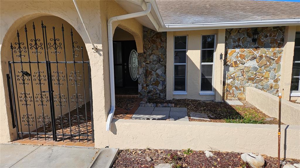 The exterior of a house features a gated courtyard, stone siding, and a front entrance — 8533 VIVA VIA DRIVE, HUDSON, FL
