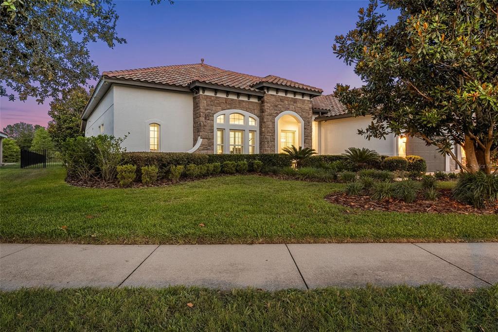 A single-story house with a stone facade, arched entryway, and a tiled roof at dusk — 17425 VARONA PLACE, LUTZ, FL