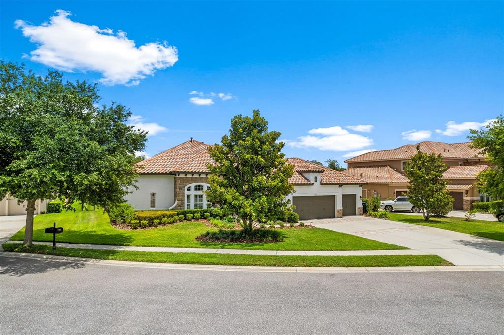 A single-story house with a tile roof, stone accents, and a three-car garage — 17425 VARONA PLACE, LUTZ, FL