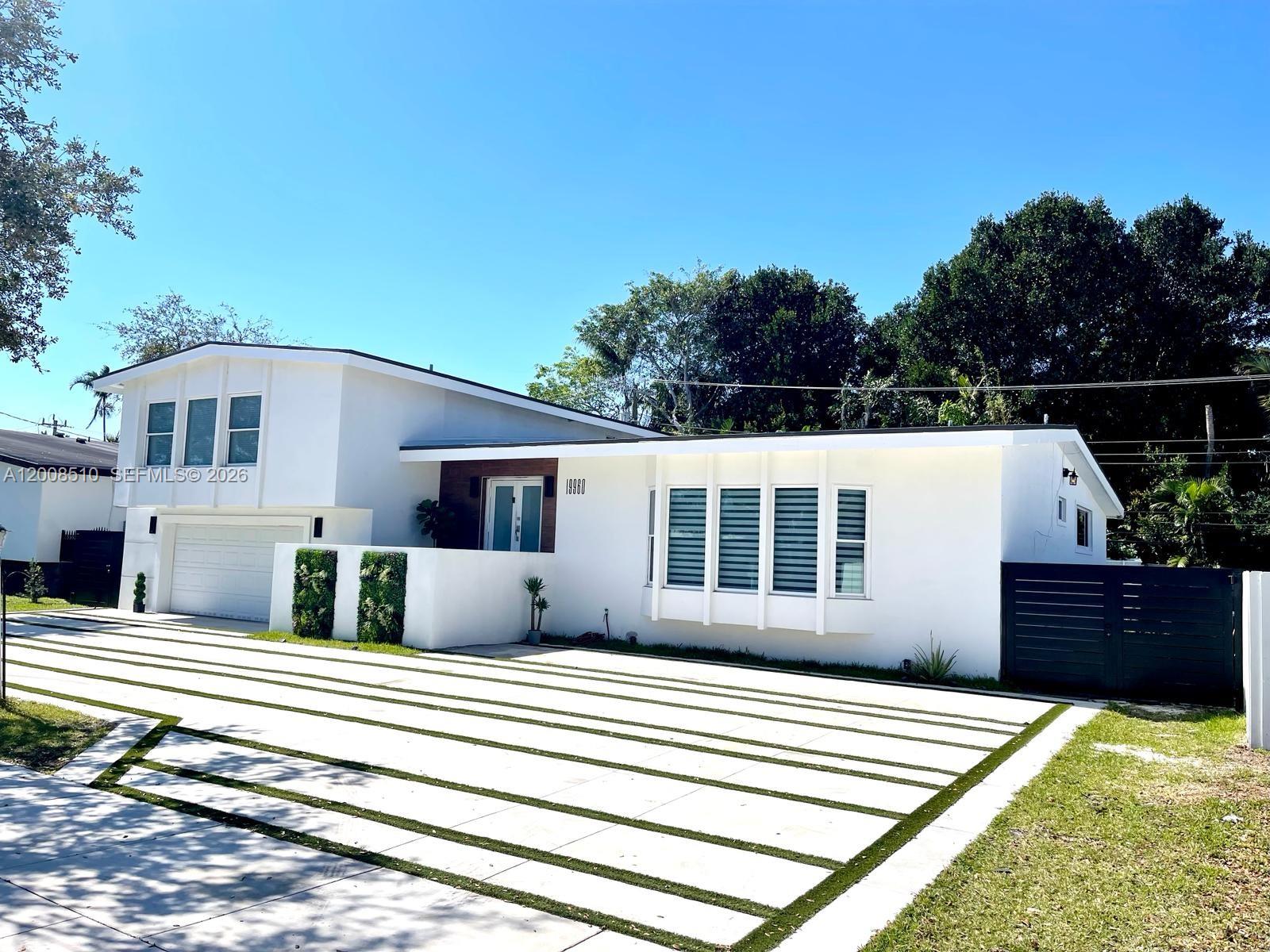 A white modern house features a large driveway with grass strips and a bay window — 19960 Highland Lakes Blvd, Miami FL 33179, MIAMI, FL