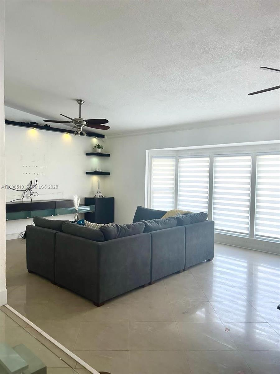 A living room features a large gray sectional sofa, a ceiling fan, and bay windows — 19960 Highland Lakes Blvd, Miami FL 33179, MIAMI, FL