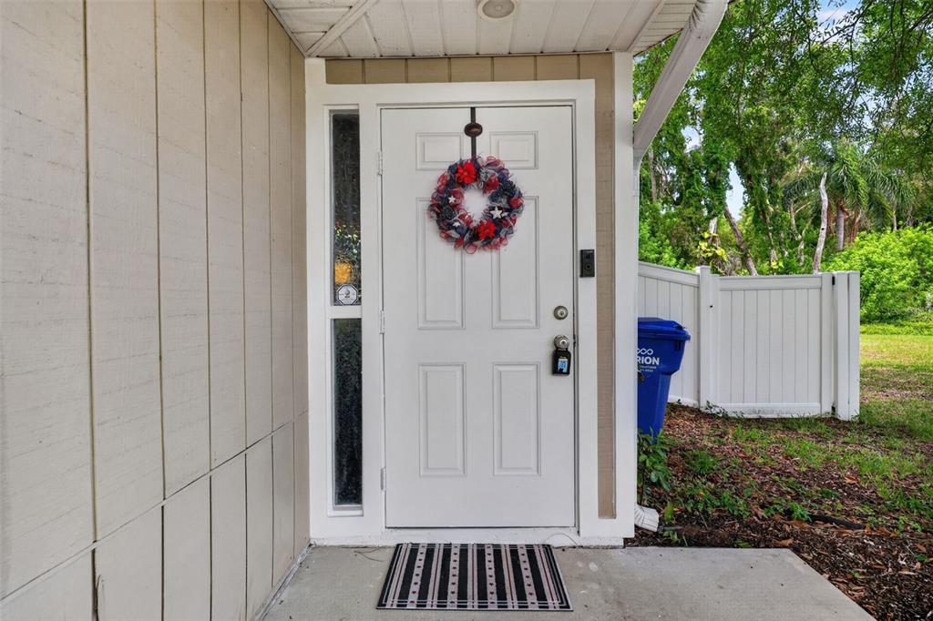A white front door with a patriotic wreath sits under a porch next to siding — 9 FRESHWATER DRIVE, PALM HARBOR, FL