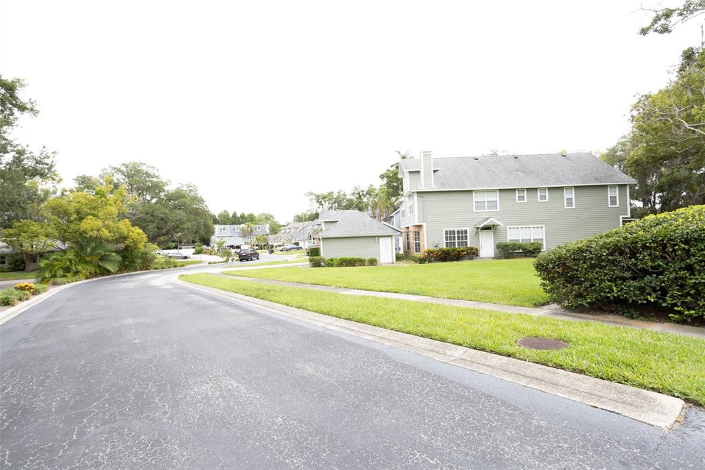 A street view of a residential neighborhood with a two-story green house and lawn — 2740 HAMBLE VILLAGE LANE, PALM HARBOR, FL
