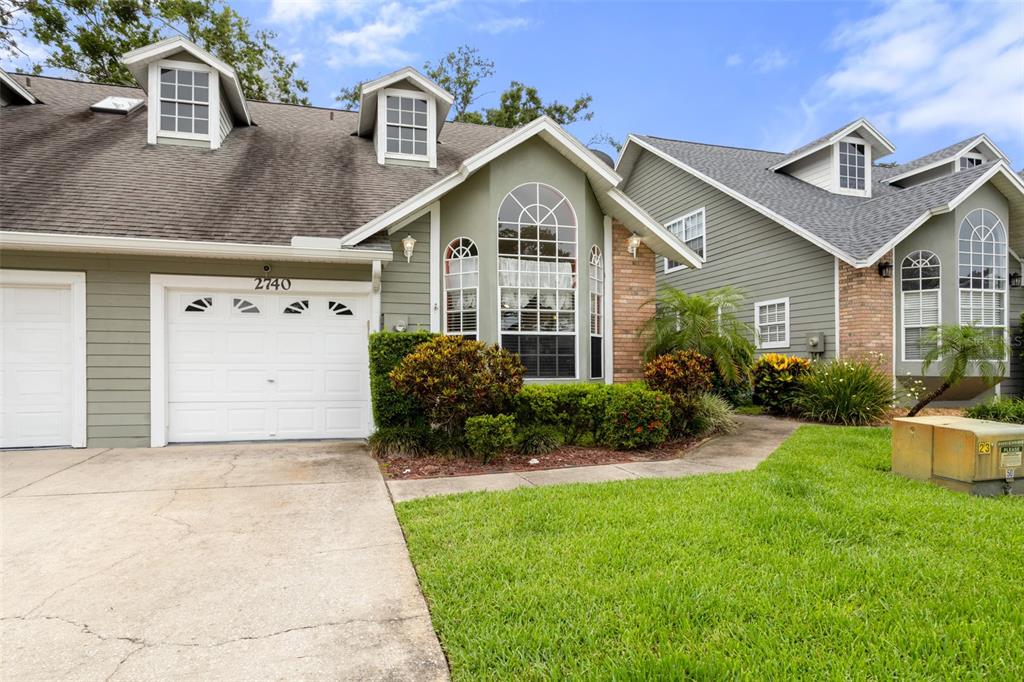 A two-story house with green siding, a white garage door, and multiple dormer windows — 2740 HAMBLE VILLAGE LANE, PALM HARBOR, FL