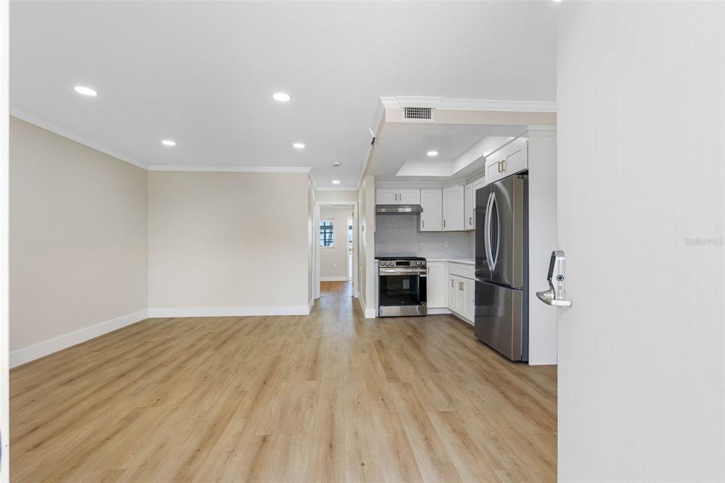 A bright, open-concept kitchen and living area features light wood flooring and white cabinetry — 1 GATESHEAD DRIVE UNIT B108, DUNEDIN, FL