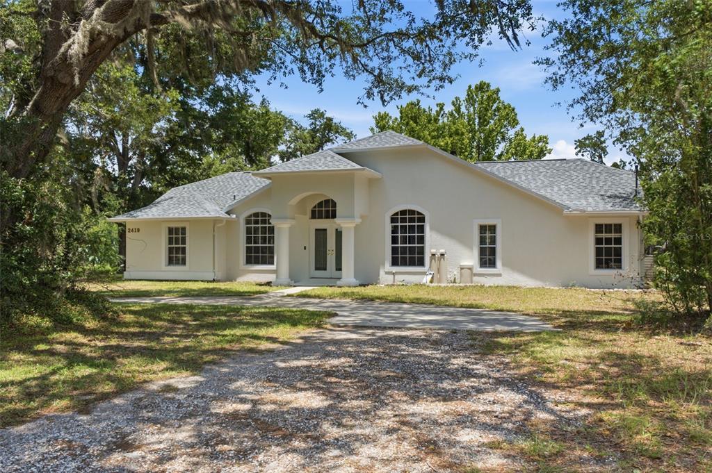 A single-story house with a light-colored stucco exterior, a gray shingled roof, and arched windows — 2419 E STAGE COACH TRAIL, INVERNESS, FL
