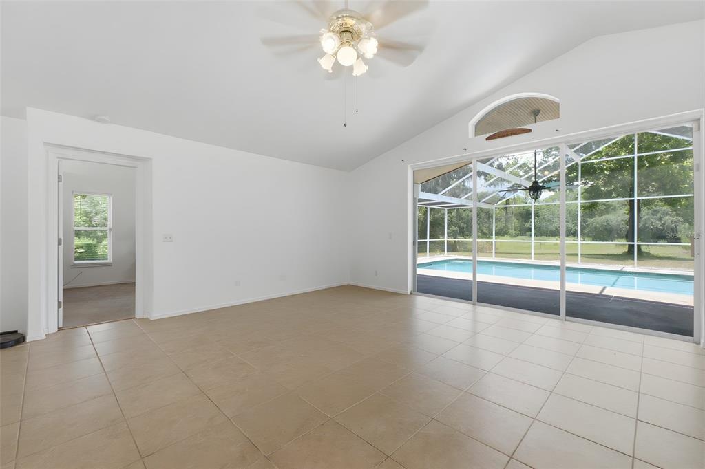A bright, tiled living room features a vaulted ceiling, ceiling fan, and sliding glass doors — 2419 E STAGE COACH TRAIL, INVERNESS, FL