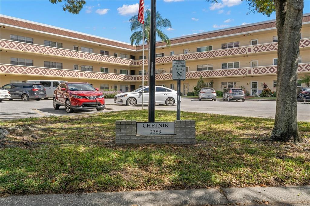 A low-rise apartment building with a parking lot and a sign reading CHETNIK 2383 — 2383 NETHERLANDS DRIVE UNIT 57, CLEARWATER, FL