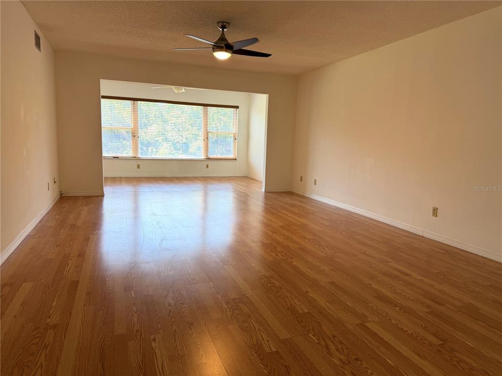 An empty living room features light-colored walls, a ceiling fan, and hardwood flooring — 2383 NETHERLANDS DRIVE UNIT 57, CLEARWATER, FL